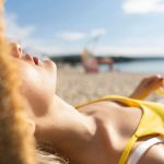 Djevojka u žutom toplesu se sunča na plaži.
