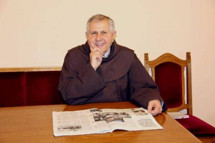 Svećenik fra Vjenceslav Janjić sjedi za stolom i čita novine.