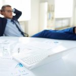 Birokratski službenik opušteno uvaljen u fotelju s nogama na stolu.