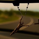 Krunica visi s retrovizora automobila, nagnuta zbog zavoja u vožnji. Isus, prikazan kao stvaran ljudski lik, otkinut je s križa i objeručke se drži za krunicu iznad križa, kao da ga inercija pokušava odbaciti. U pozadini se kroz vjetrobransko staklo vidi zamućena zavojita cesta.