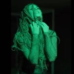 Mlada pjevačica Anami u zeleno osvijetljenom kadru iz glazbenog spota “Fobije”, s pletenicama i reflektirajućim kostimom.