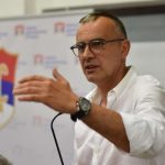 Političar Babalj za govornicom u bijeloj košulji s podignutom rukom na kojoj je sat