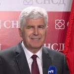 Dragan Čović govori na konferenciji za medije ispred SNSD pozadine s crvenom zastavom.