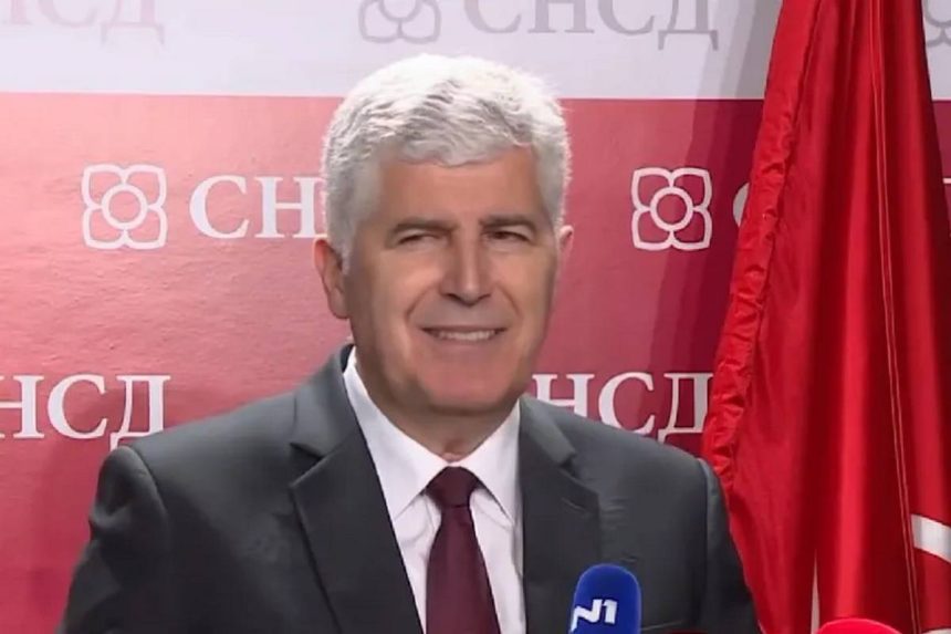 Dragan Čović govori na konferenciji za medije ispred SNSD pozadine s crvenom zastavom.