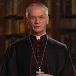 Zagrebački nadbiskup Dražen Kutleša pripriopćenju za televiziju. U pozadini regal s knjigama.