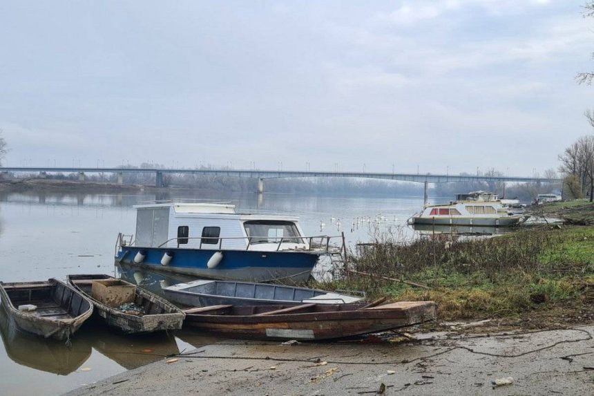 Čamci i brodice privezani uz obalu na rijeci Savi kod Orašja. U pozadini se vidi most na Savi.