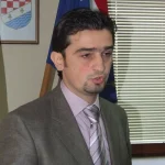 Željko Josić za govornicom. U pozadini zastava i grb Županje Posavske.