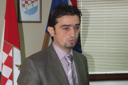 Željko Josić za govornicom. U pozadini zastava i grb Županje Posavske.