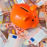 Razasute novčanice u apoenima od 50 eura, na njima stoji narandžasta štedna kasica.