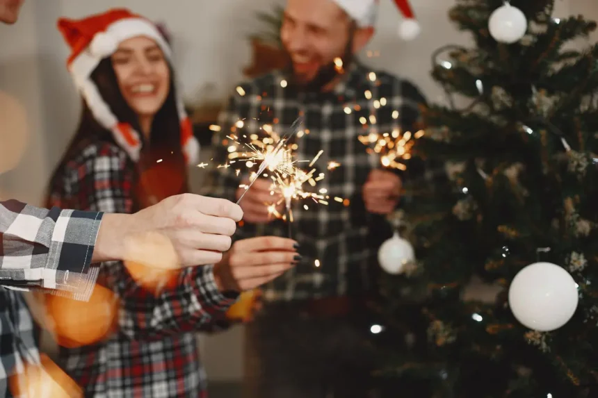 Muškarac i žena u novogodišnjem raspoloženju pored okićenog bora u ruci drže prskalice.