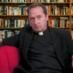 Svećenik Josip Mužić sjedi u crvenoj fotelji, u pozadini regal s knjigama.