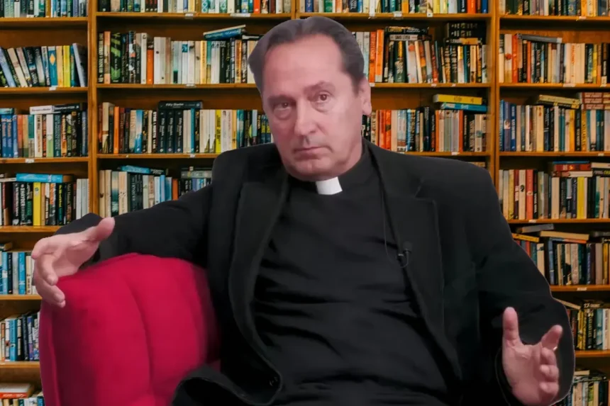 Svećenik Josip Mužić sjedi u crvenoj fotelji, u pozadini regal s knjigama.