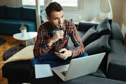 Čovjek u šarenoj košulji zamišljeno sjedi uz laptop.