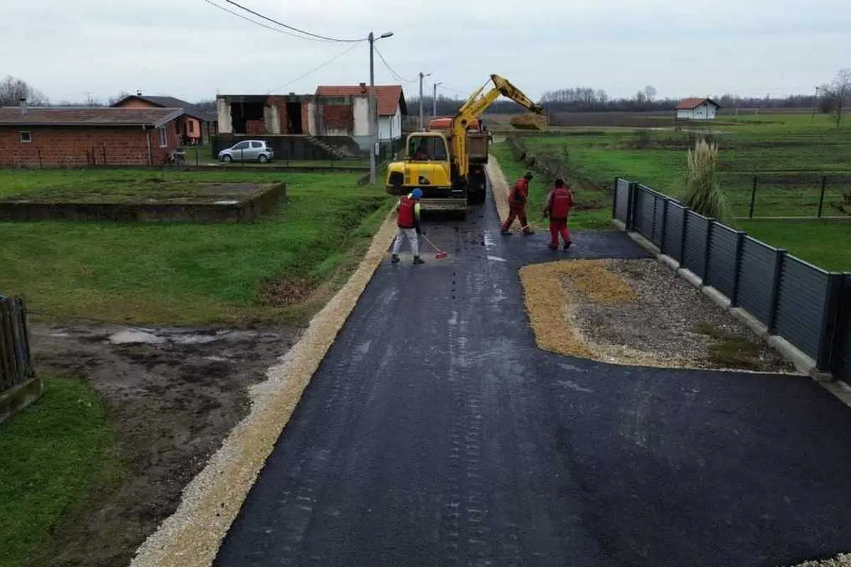 Prostiranje asfalta u ravnici. Ruralni pejzaž, s kamionom u sredini i radnicima s lopatama.