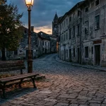 Prazna klupa u malom mjestu, predvečer, tišina, prazna ulica u pozadini, osjećaj odumiranja zajednice.