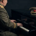 Maršalska figura u svečanoj odori svira klavir, dok na instrumentu stoji oficirska šapka s crvenom zvijezdom.